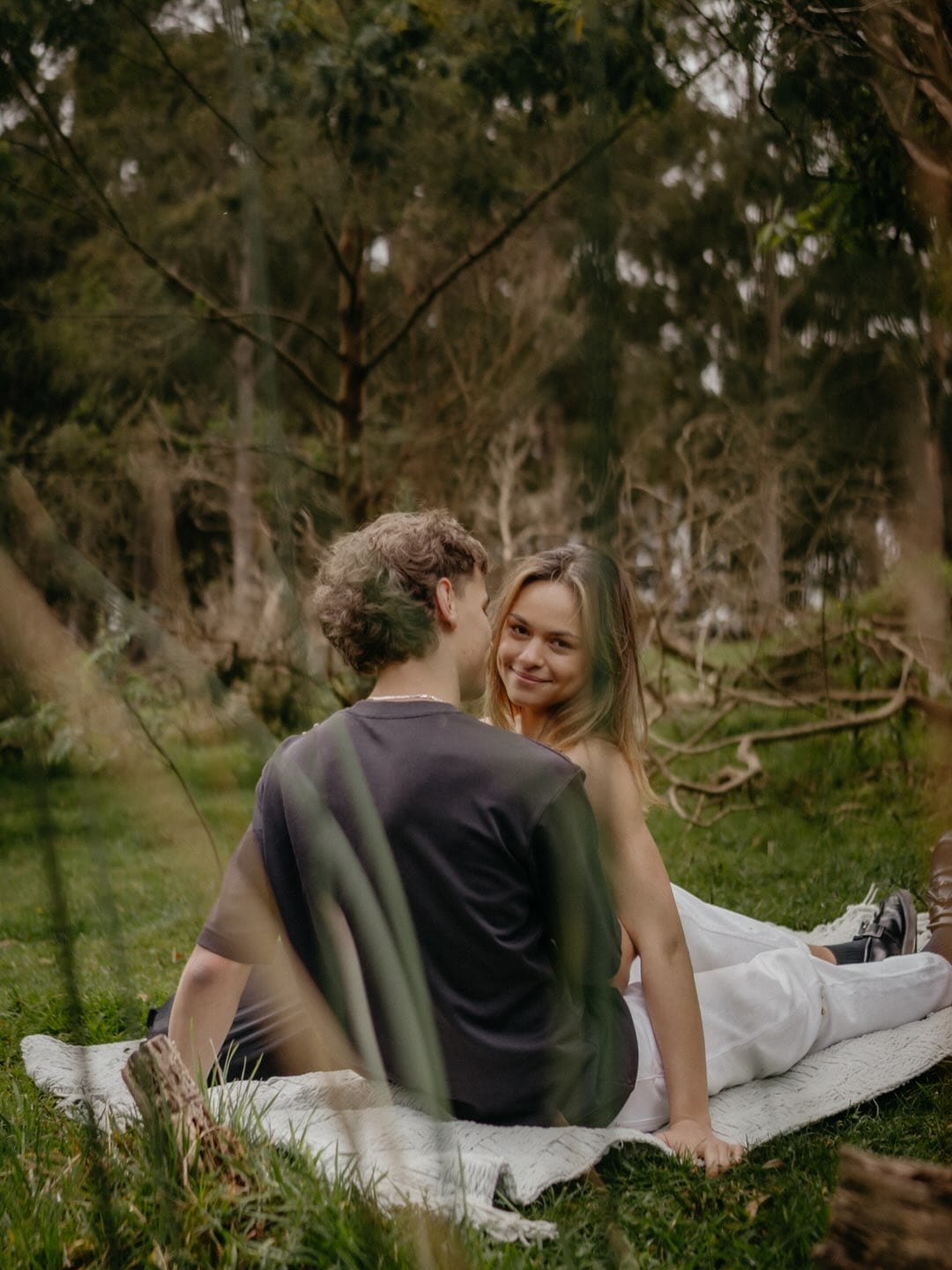 Sophie and Alex sitting together on a picnic blanket among the trees