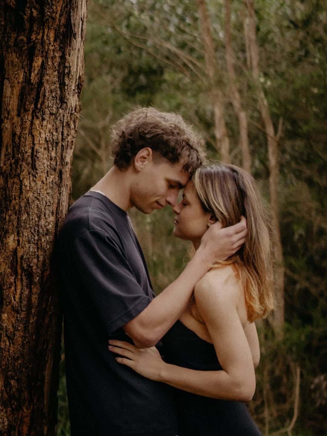 Sophie and Alex leaning close beside a tree in the bush